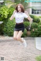 A woman in a white shirt and black skirt jumping in the air.