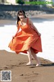 A woman in an orange dress is walking on the beach.