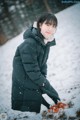 A woman in a black coat crouching down in the snow.