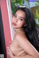 A woman with long black hair leaning against a red wall.