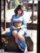 A woman in a blue kimono sitting on a wooden bench.