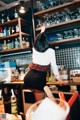 A woman standing behind a bar with a lot of bottles on the shelves.