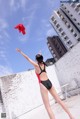 A woman in a black and red bathing suit throwing a red scarf.